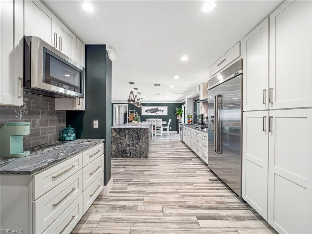 Kitchen with light stone countertops, hanging light fixtures, stainless steel appliances, white cabinets, and light wood-type flooring