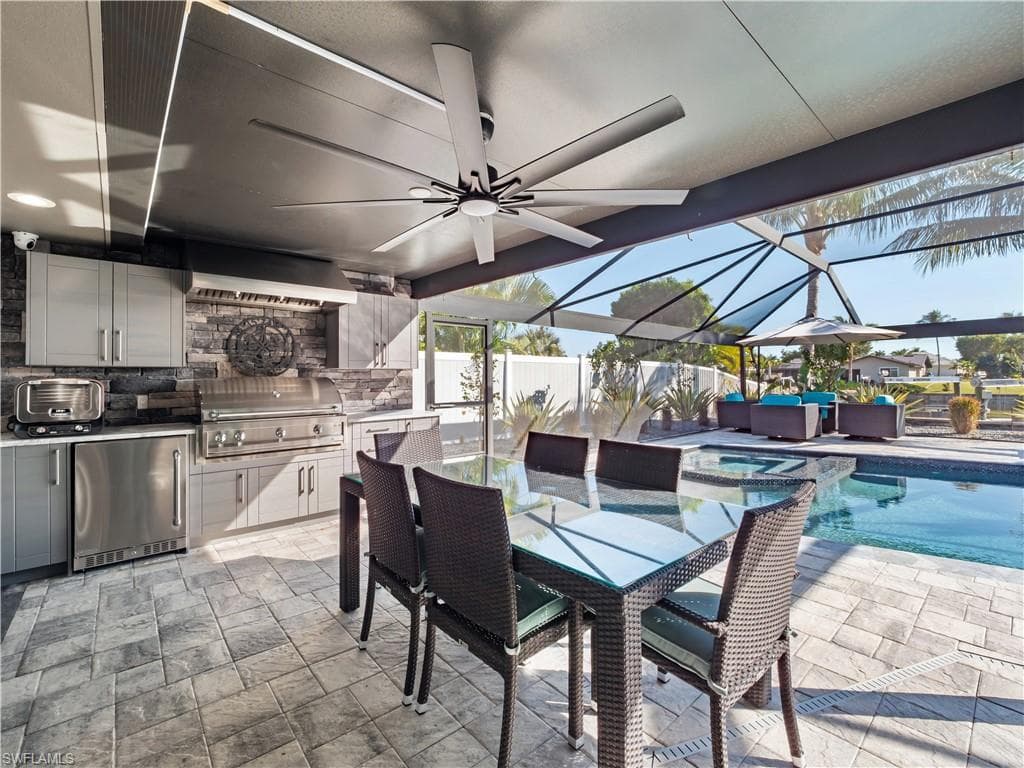 View of patio / terrace featuring an outdoor kitchen / dining area, a sunroom, a pool with connected hot tub, a ceiling fan, and a lanai