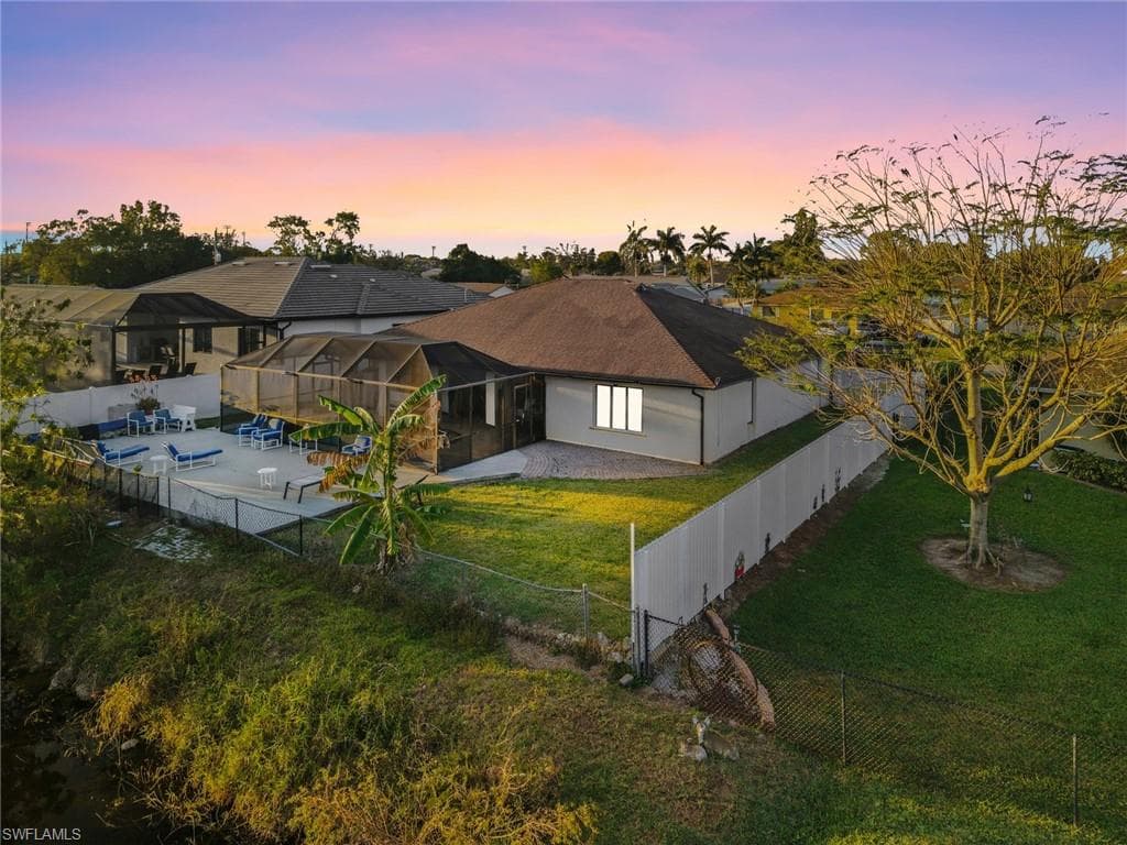 Back of property at dusk featuring a fenced backyard, glass enclosure, a sunroom, and a patio