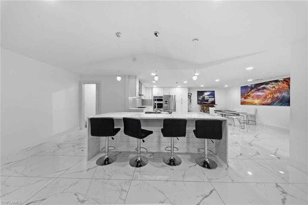 Kitchen with light stone counters, a kitchen bar, white cabinets, decorative light fixtures, and a large island