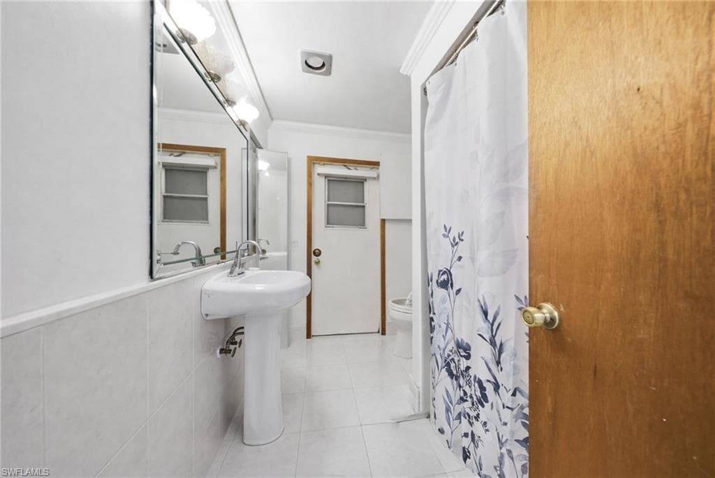 Full bath featuring ornamental molding, a shower with shower curtain, and light tile patterned floors