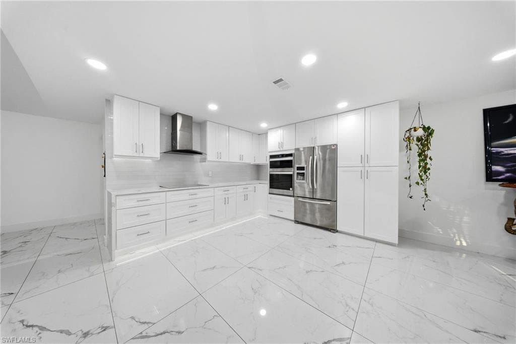 Kitchen with white cabinets, stainless steel appliances, decorative backsplash, light marble finish floors, and recessed lighting