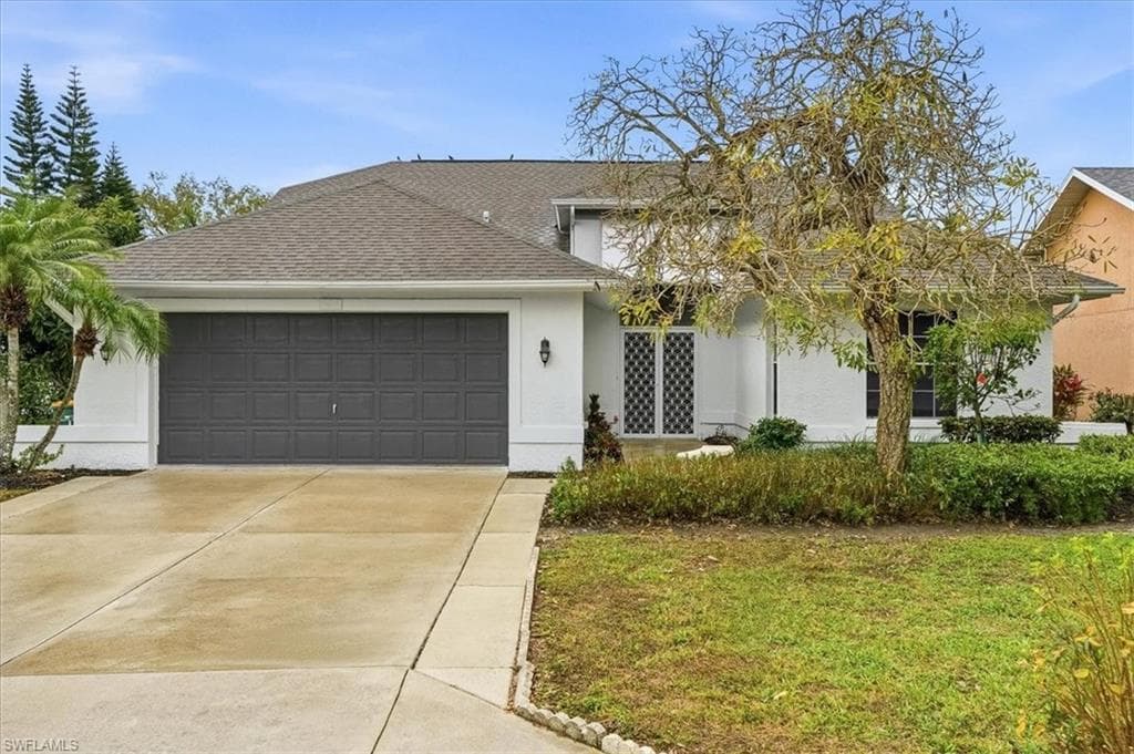 View of front of home with a shingled roof, an attached garage, concrete driveway, stucco siding, and a front lawn