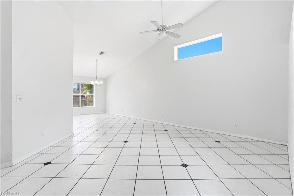 Empty room featuring vaulted ceiling, ceiling fan, suspended lighting, and light tile patterned floors