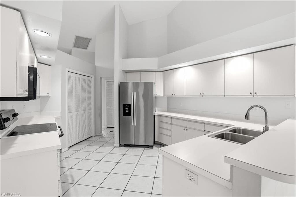 Kitchen with stainless steel fridge with ice dispenser, white range oven, light countertops, a high ceiling, and a peninsula
