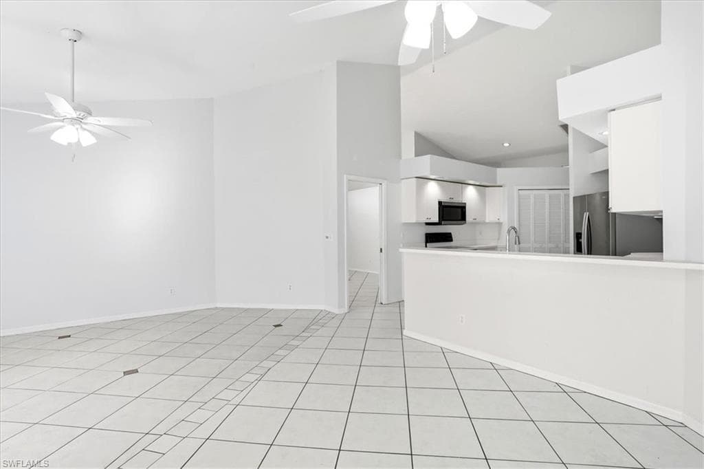 Unfurnished living room with ceiling fan, lofted ceiling, and light tile patterned floors