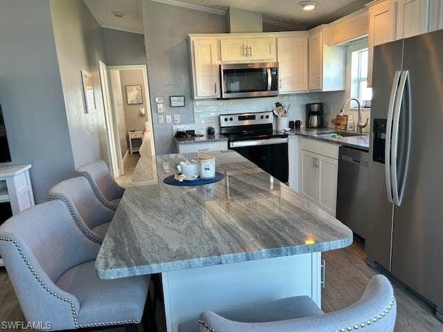 Kitchen with stainless steel appliances, white cabinets, dark stone counters, crown molding, and decorative backsplash