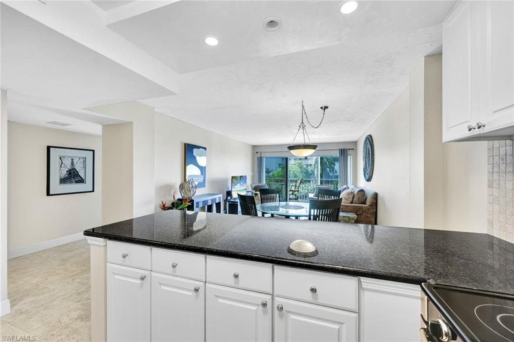 Kitchen with white cabinetry, dark stone counters, open floor plan, electric range oven, and decorative light fixtures