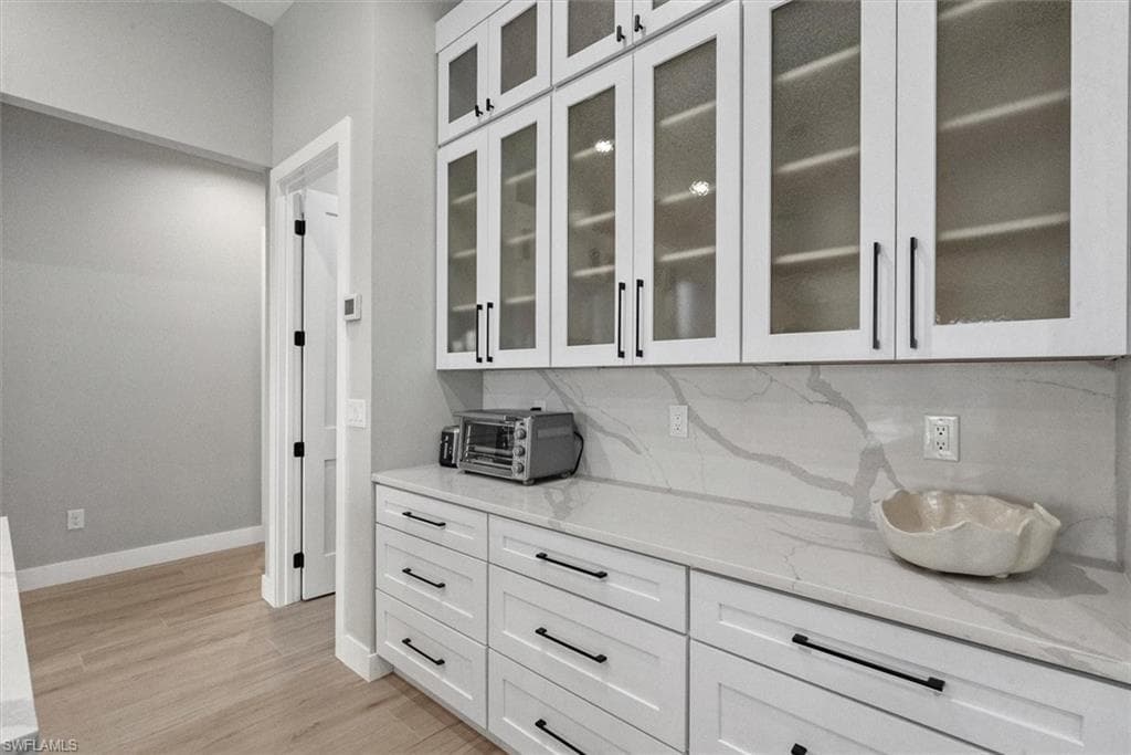 Bar with white cabinetry, light stone countertops, glass insert cabinets, and light wood-style floors