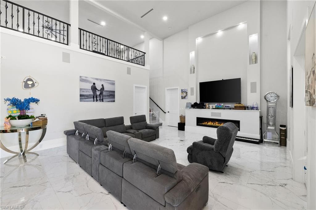 Living room featuring a warm lit fireplace, recessed lighting, a high ceiling, and light marble finish flooring