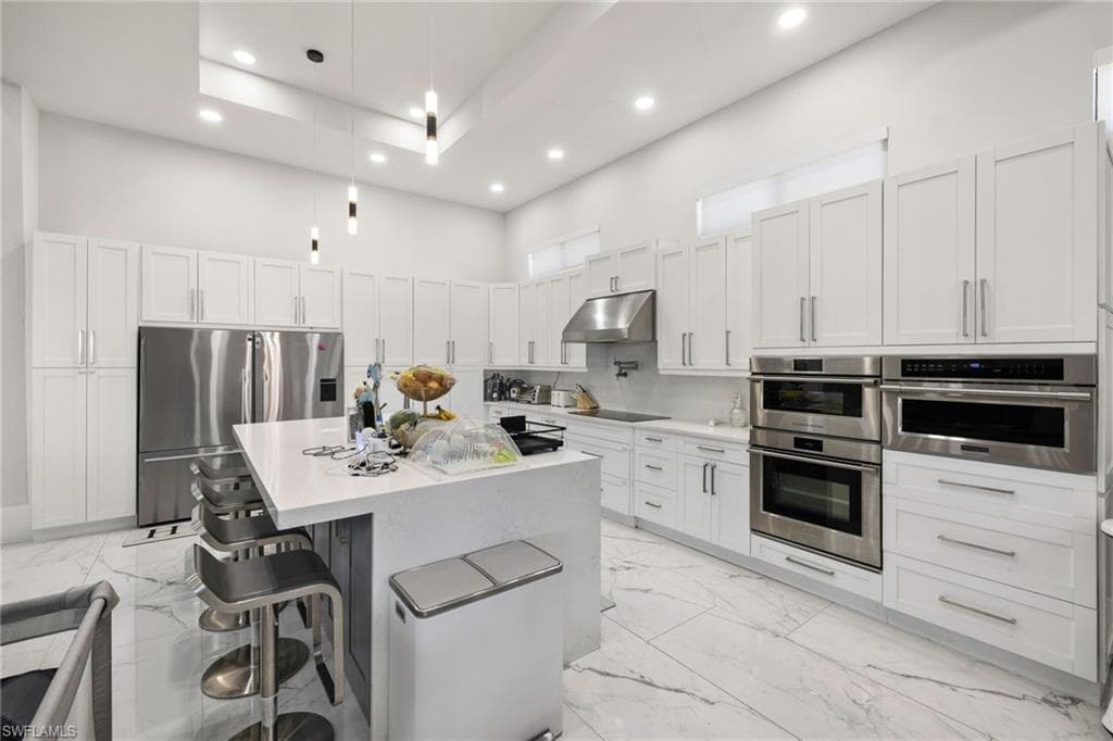 Kitchen with a center island, stainless steel appliances, light stone counters, a kitchen bar, and pendant lighting