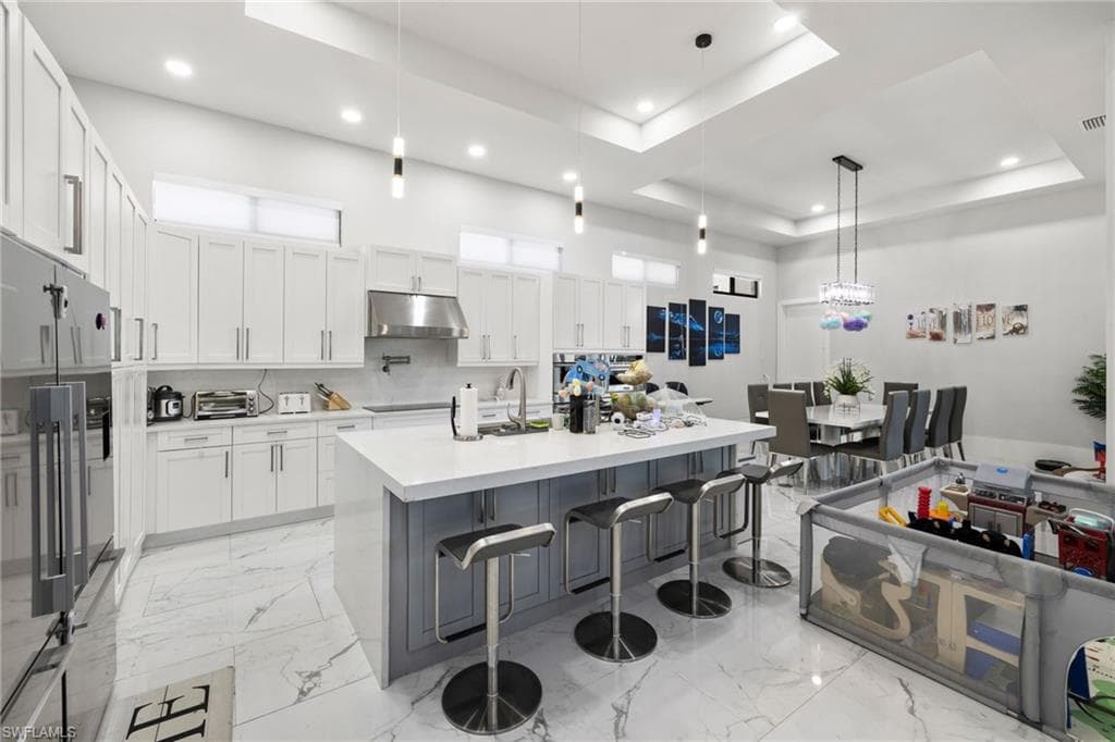 Kitchen featuring high quality fridge, a large island with sink, decorative light fixtures, a kitchen bar, and a tray ceiling