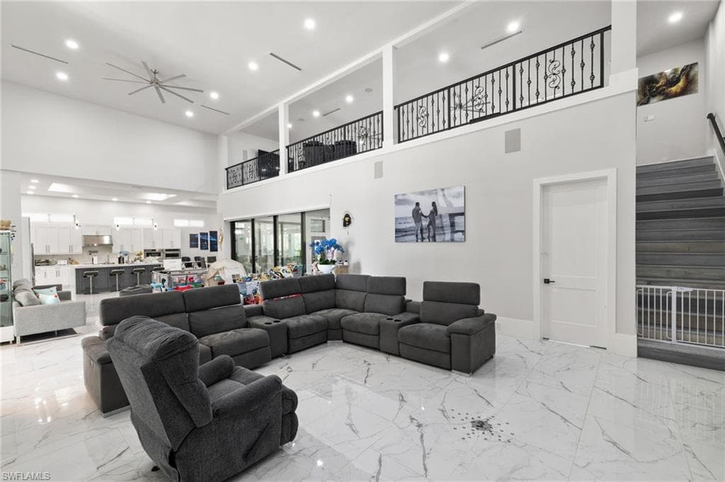 Living room featuring recessed lighting, a ceiling fan, light marble finish flooring, and a high ceiling