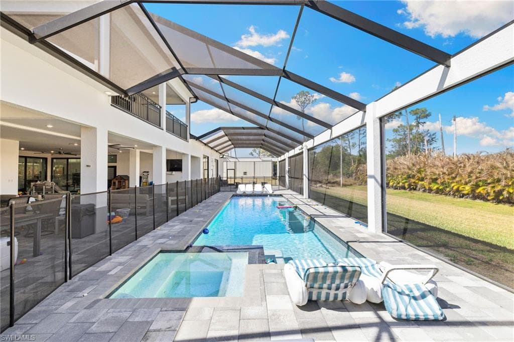Relaxing pool / spa with a sunroom, glass enclosure, a lawn, and a patio