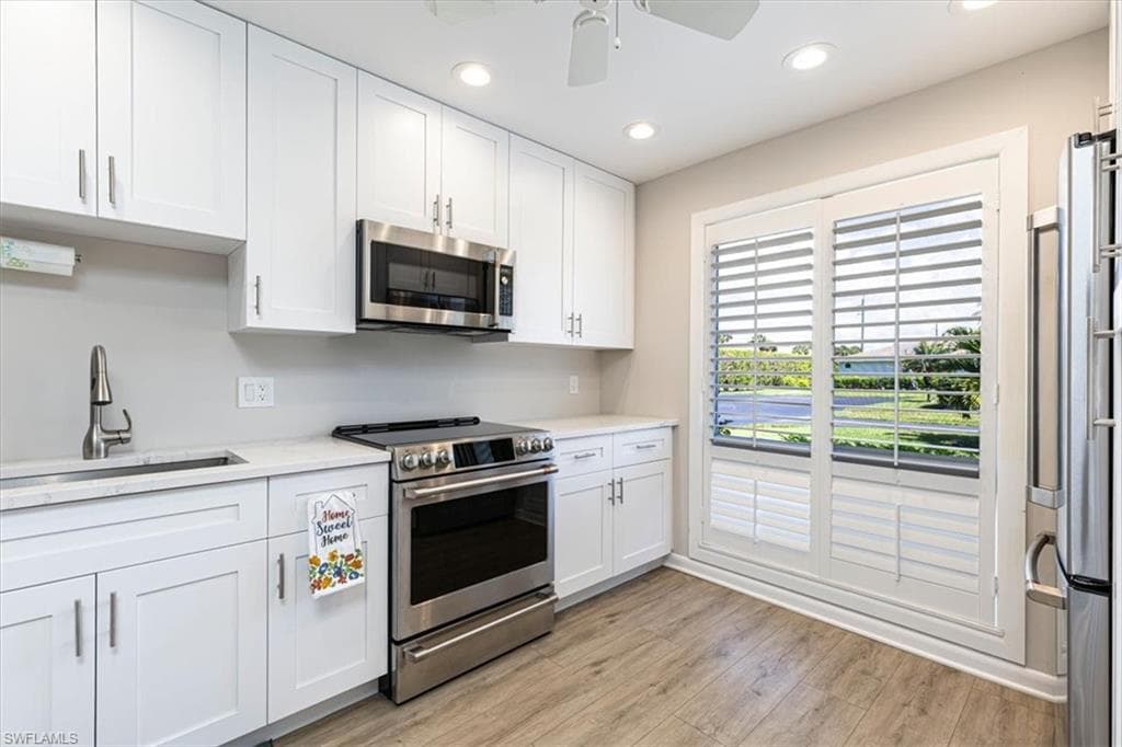 Kitchen featuring stainless steel appliances, white cabinetry, recessed lighting, a ceiling fan, and light wood-style flooring