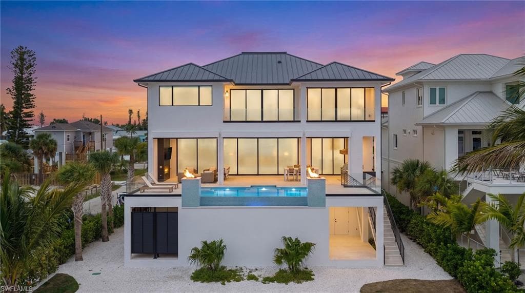 Modern multi-story residence featuring a dark metal roof, white exterior, and extensive floor-to-ceiling windows