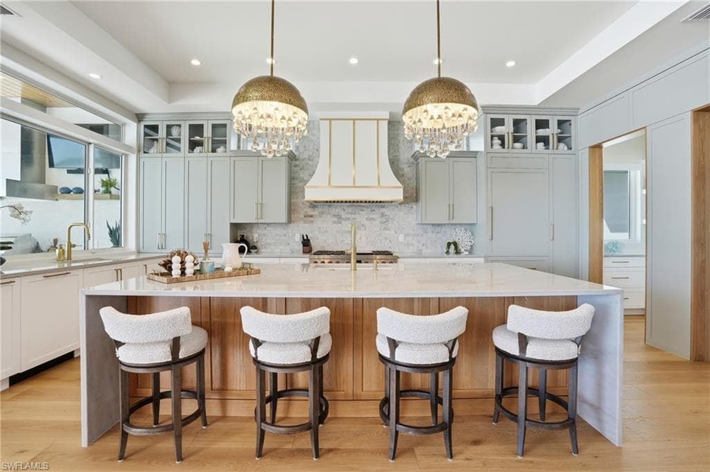 Dual tone kitchen featuring glass insert cabinets, a breakfast bar, light wood finished floors, and dual tone cabinetry - Virtually Edited Image
