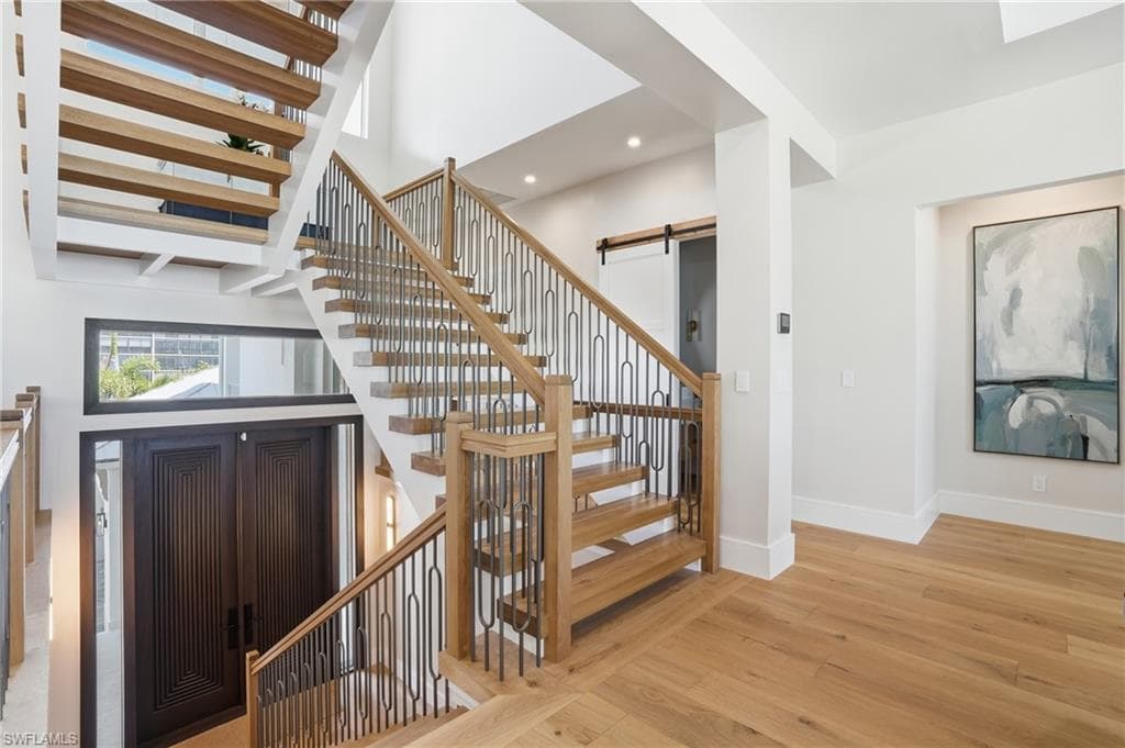 Staircase featuring a barn door, wood-type flooring, a high ceiling, and recessed lighting - Virtually Edited Image