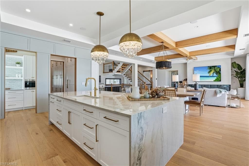 Kitchen featuring white cabinetry, hanging lights, light stone countertops, open floor plan, and a large island with sink - Virtually Edited Image