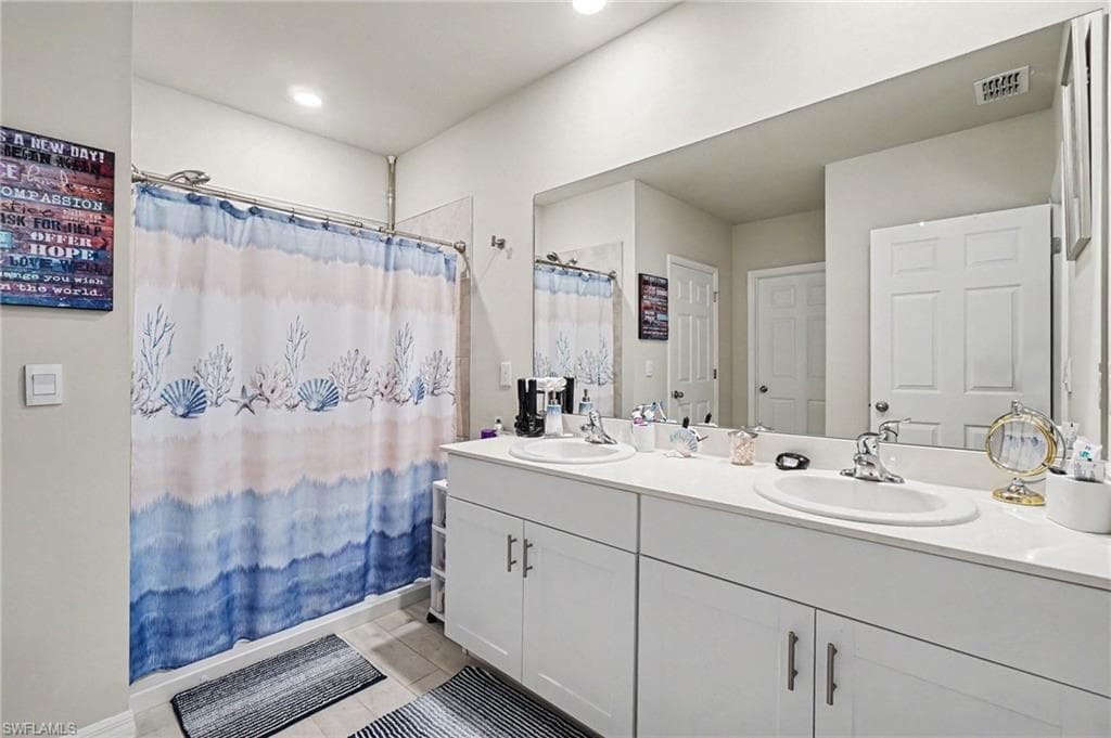 Bathroom with double vanity, curtained shower, and light tile patterned floors