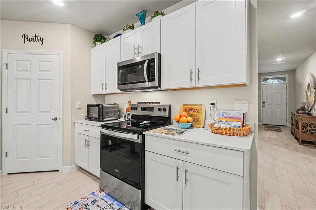 Kitchen with stainless steel appliances, light countertops, white cabinetry, and recessed lighting