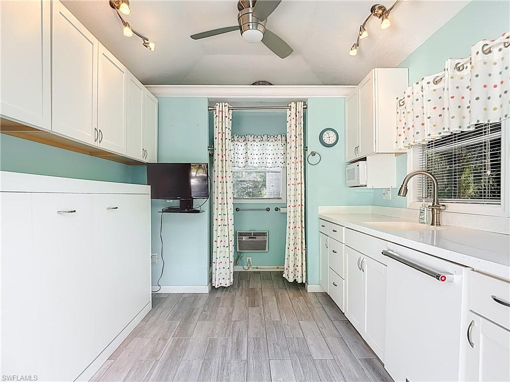 Kitchen featuring white cabinets, rail lighting, a ceiling fan, white dishwasher, and vaulted ceiling