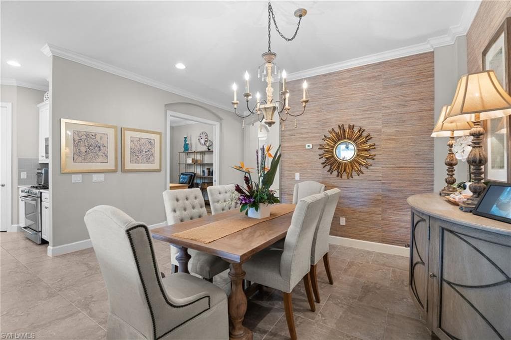 Dining space featuring crown molding, a chandelier, arched walkways, and an accent wall