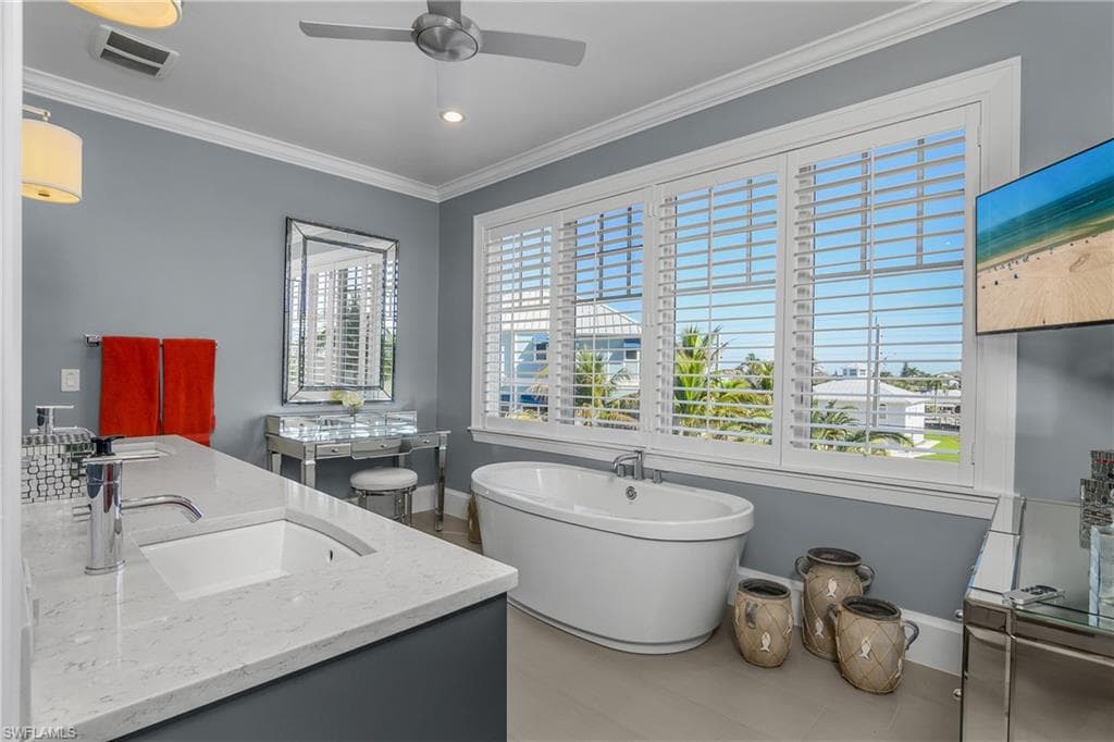 Full bathroom featuring double vanity, ornamental molding, a soaking tub, ceiling fan, and recessed lighting