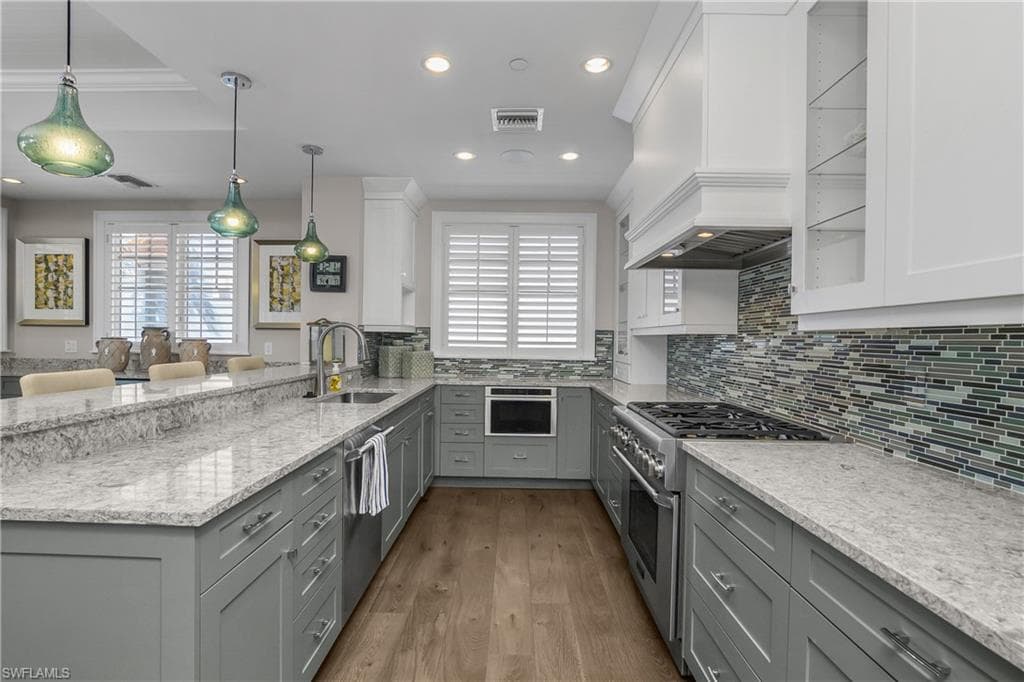 Dual tone kitchen featuring light stone countertops, a peninsula, stainless steel appliances, pendant lighting, and dark wood-style flooring