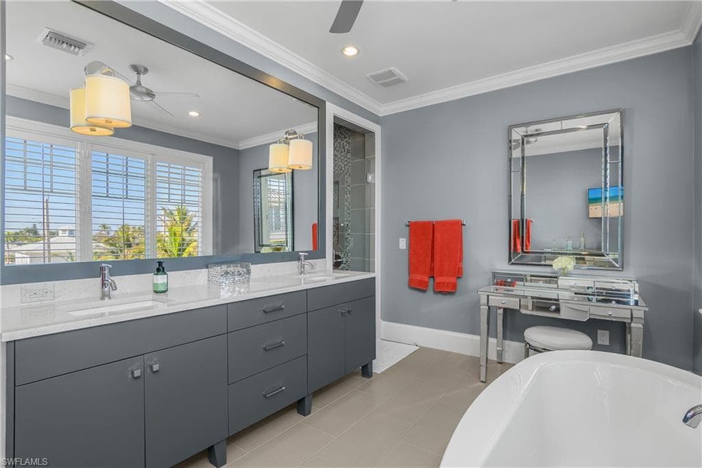 Full bath with double vanity, crown molding, a freestanding bath, a ceiling fan, and recessed lighting