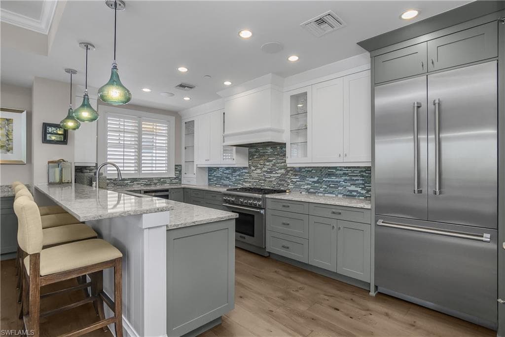 Two tone kitchen with premium appliances, decorative light fixtures, a peninsula, light stone counters, and tasteful backsplash