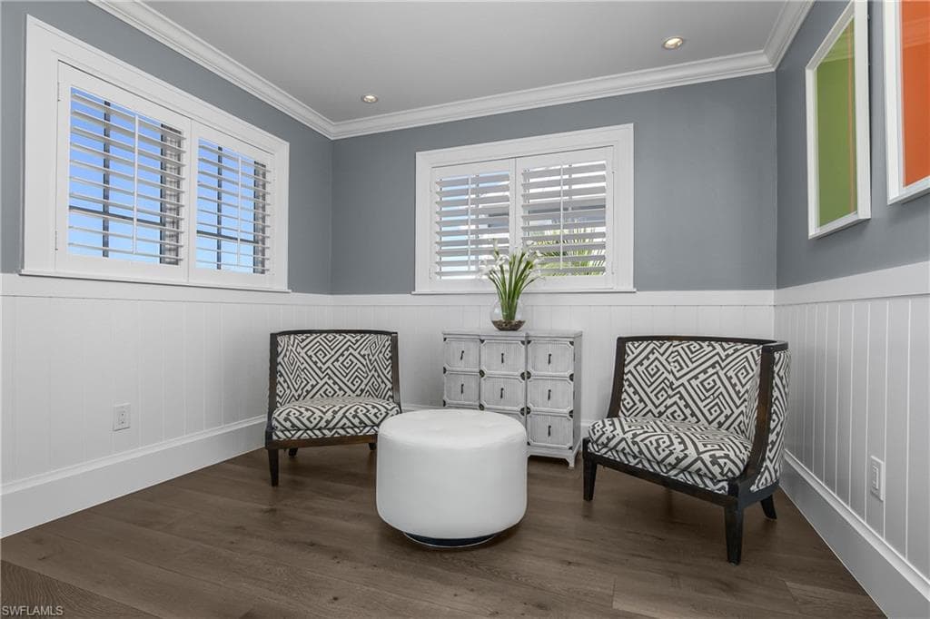 Living area with dark wood-style floors, a wainscoted wall, and crown molding