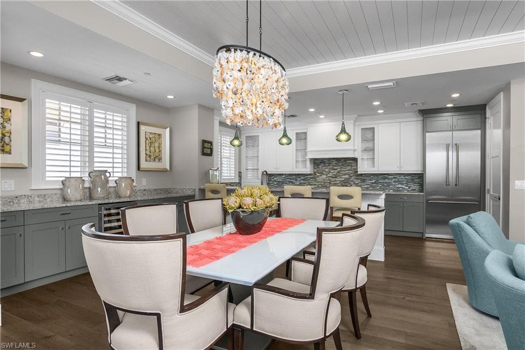 Dining space with ornamental molding, suspended lighting, dark wood-style floors, and beverage cooler