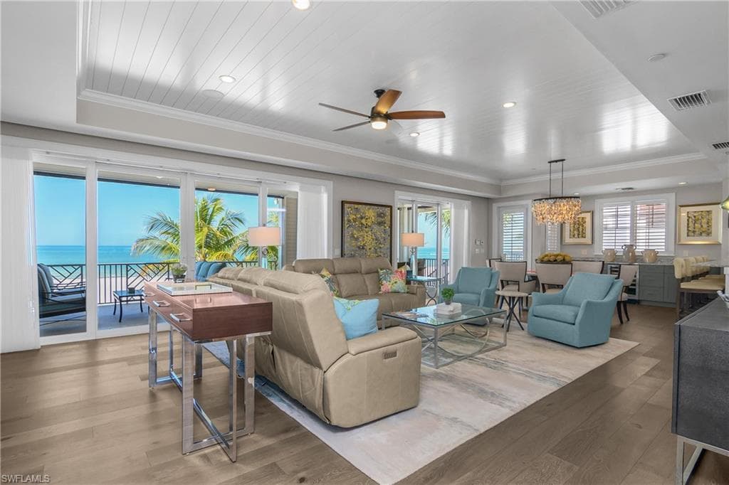 Living room featuring ceiling fan, hardwood / wood-style flooring, ornamental molding, a water view, and a raised ceiling