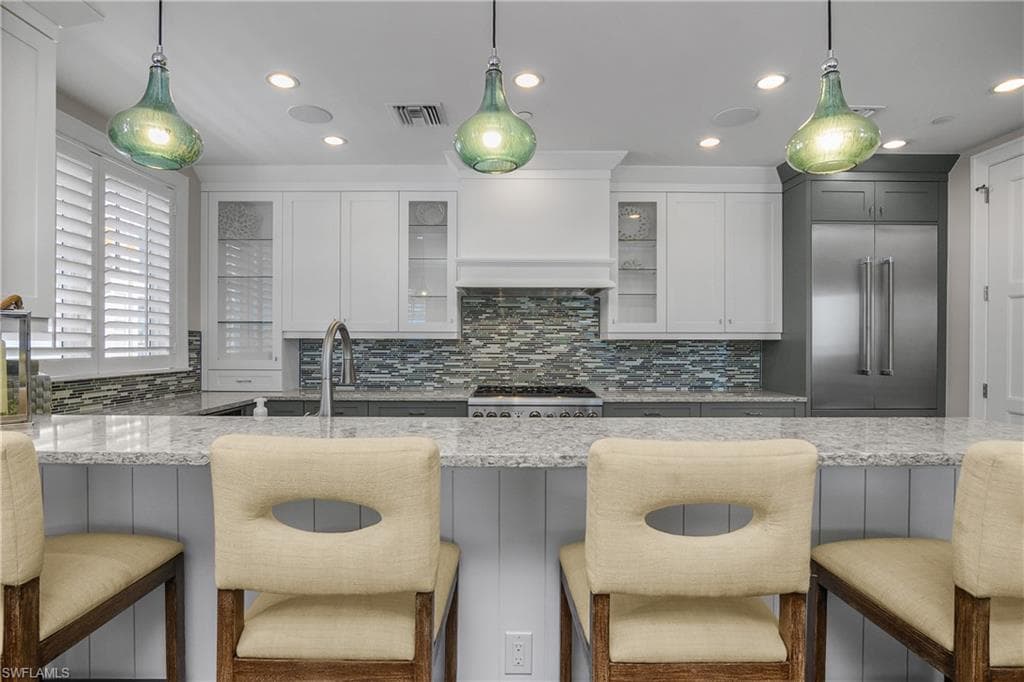 Kitchen featuring a breakfast bar area, decorative light fixtures, light stone counters, stainless steel appliances, and decorative backsplash