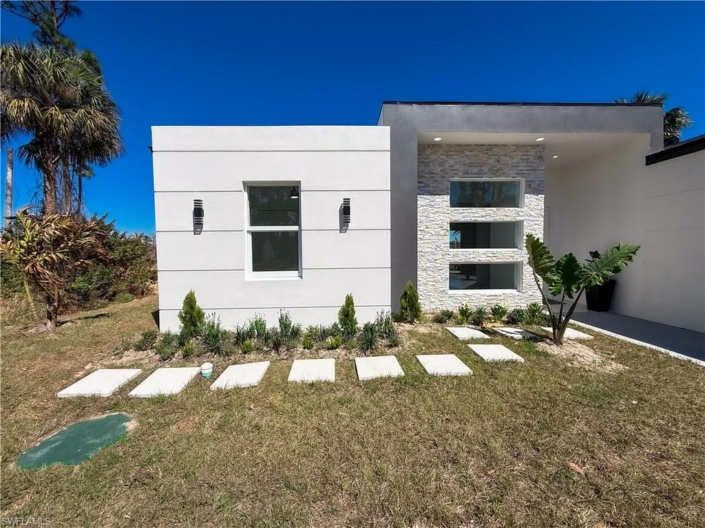 View of front facade with a front yard, stone siding, and stucco siding
