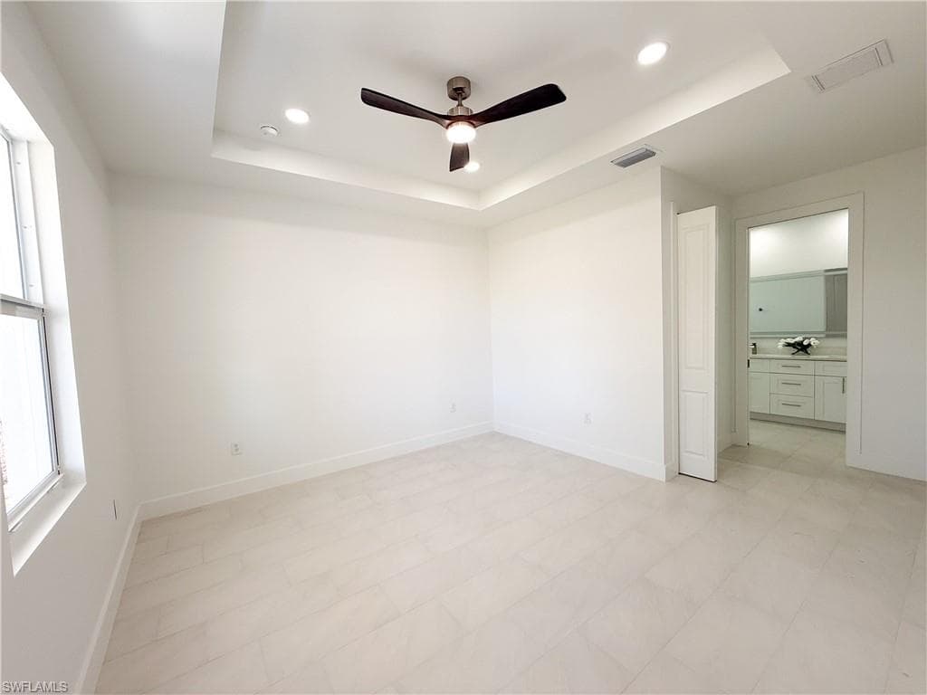 Master bedroom with a tray ceiling, ceiling fan, light floors, ensuite bath, and recessed lighting