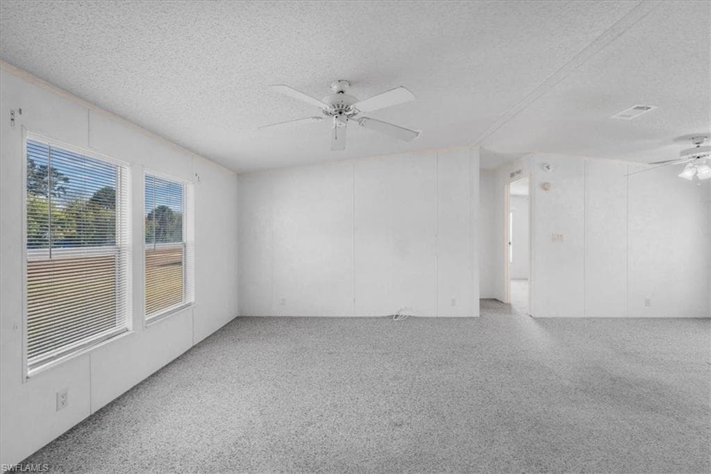 Spare room with ceiling fan, a textured ceiling, a decorative wall, and light carpet