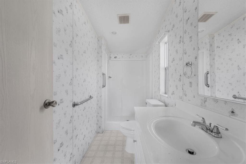 Bathroom featuring vanity, a stall shower, light floors, and wallpapered walls
