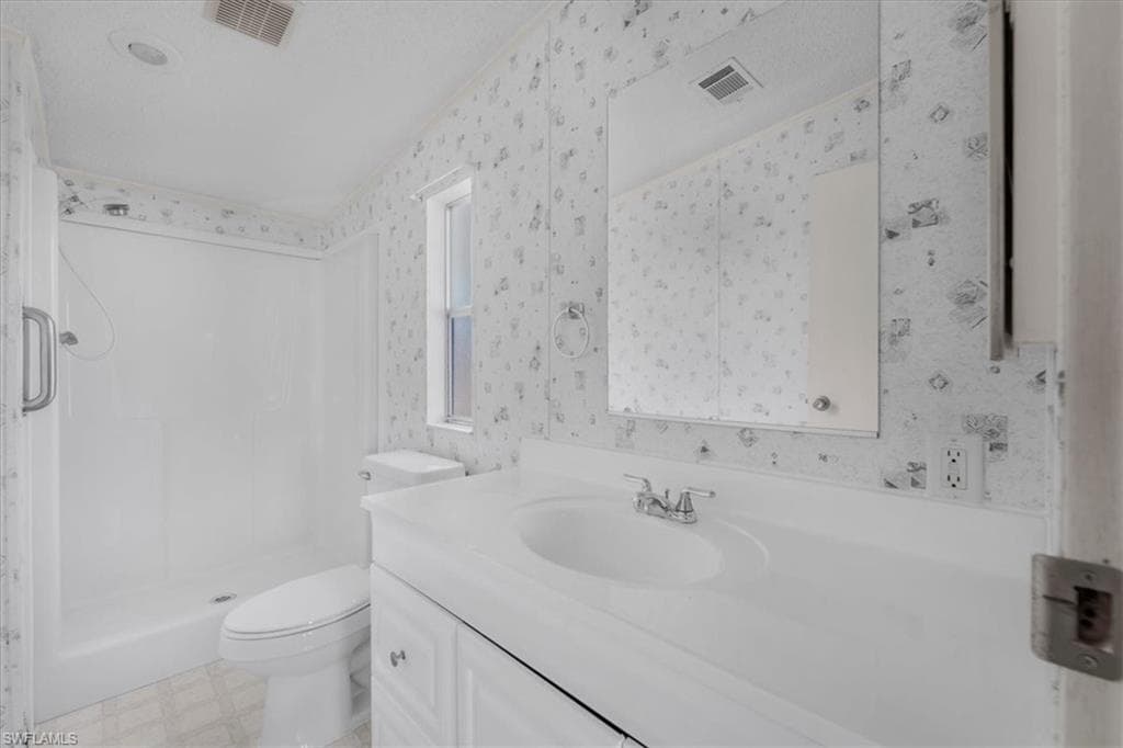 Full bathroom with vanity, light floors, a shower stall, and wallpapered walls