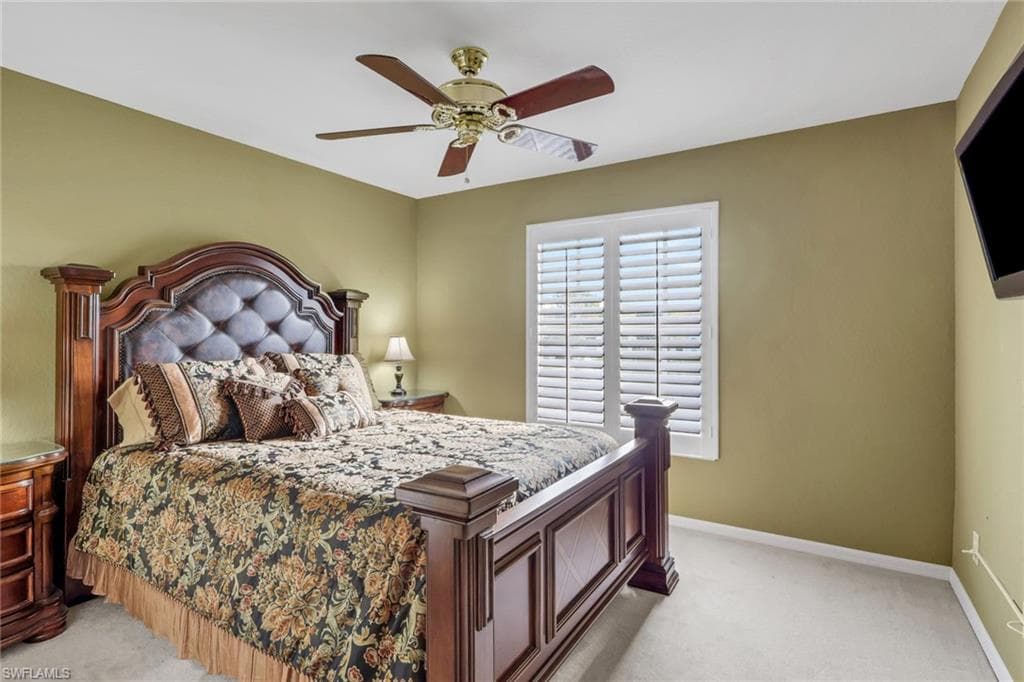 Primary bedroom with walk in closet light colored carpet, plantation shutters and ceiling fan