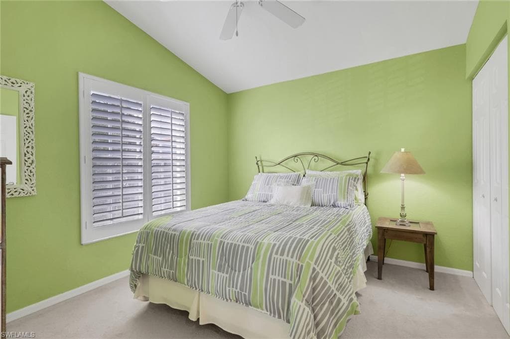 Bedroom featuring plantation shutters, walk in closet, light colored carpet, and a ceiling fan