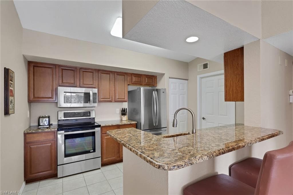 Kitchen with a peninsula, stainless steel appliances, granite counters, wood finish cabinetry, and a breakfast bar area