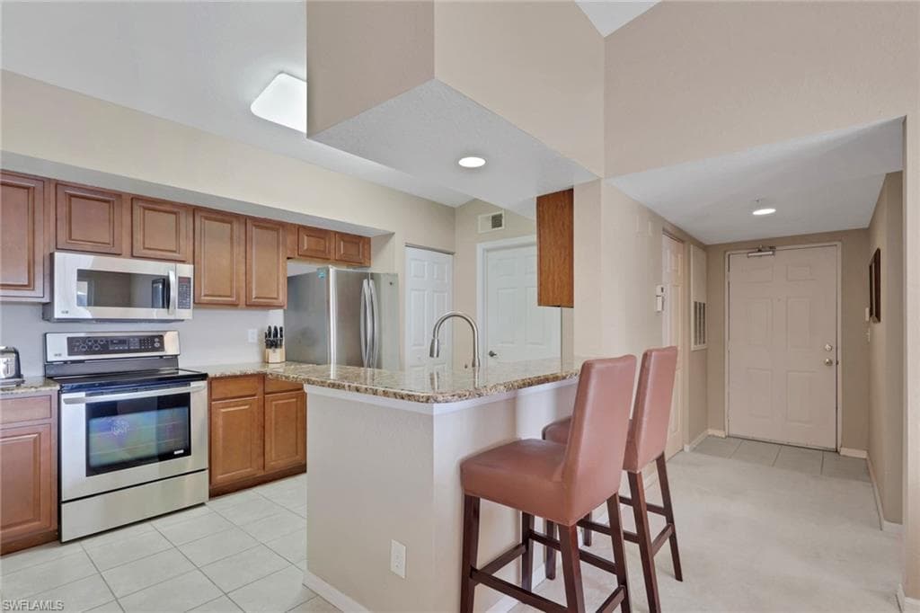 Kitchen with a breakfast bar area, stainless steel appliances, wood finish cabinets, and light stone countertops