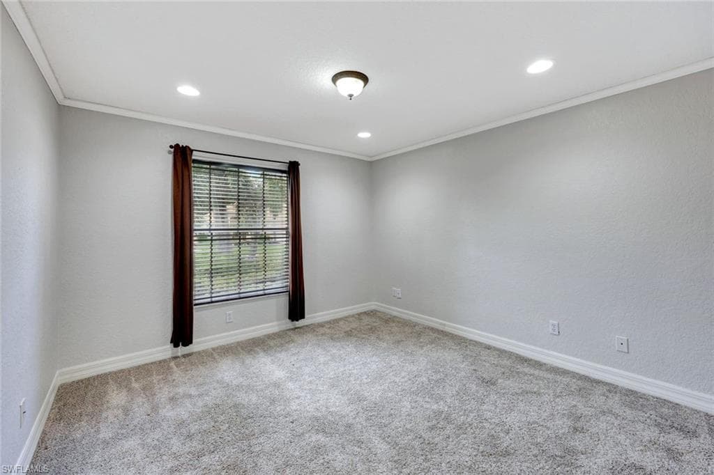 Empty room featuring light colored carpet, ornamental molding, a textured wall, and recessed lighting