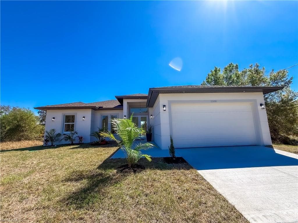 View of front of property with driveway, a garage, stucco siding, and a front lawn