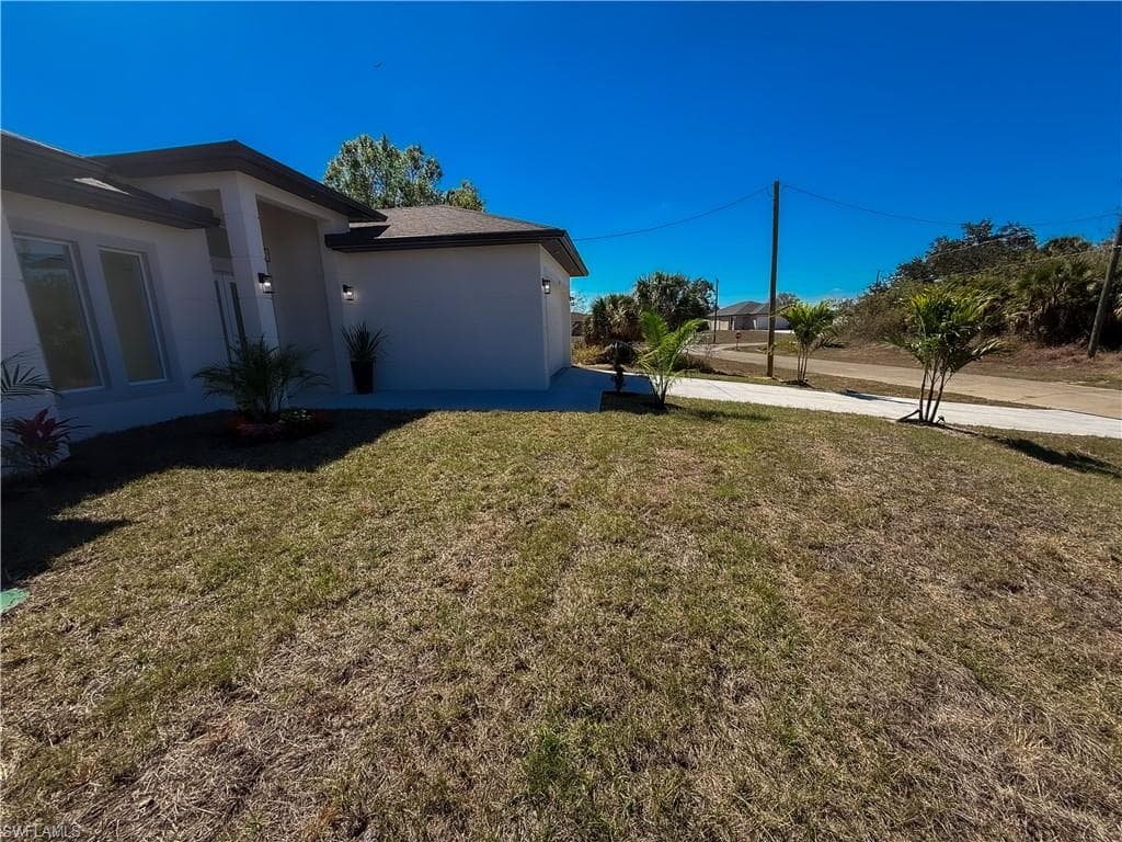 View of grassy yard featuring an attached garage and driveway