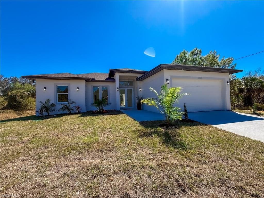 Prairie-style home with a front yard, stucco siding, an attached garage, concrete driveway, and french doors