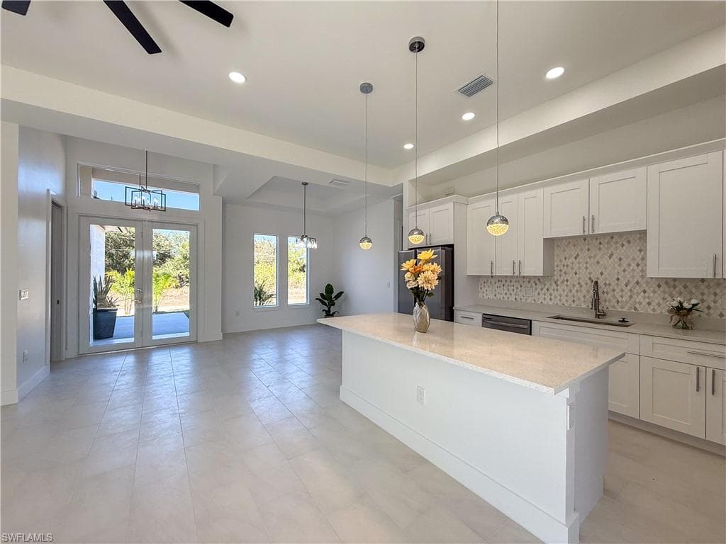 Kitchen with white cabinetry, stainless steel appliances, light stone countertops, tasteful backsplash, and a center island