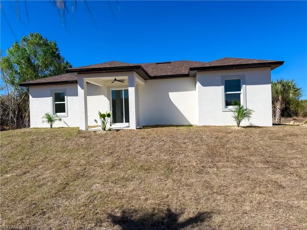Rear view of property with stucco siding, a yard, a shingled roof, and a ceiling fan